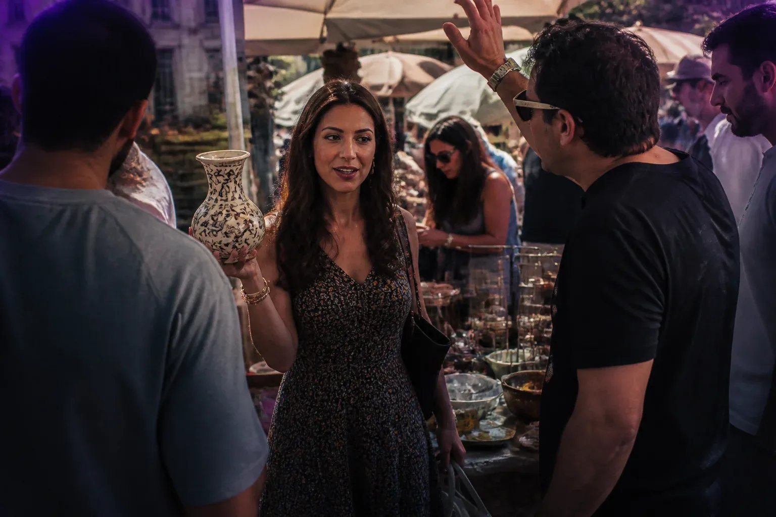 מוכרת בשוק פשפשים מרימה אגרטל קרמיקה בזמן שכמה אנשים מתקבצים סביבה