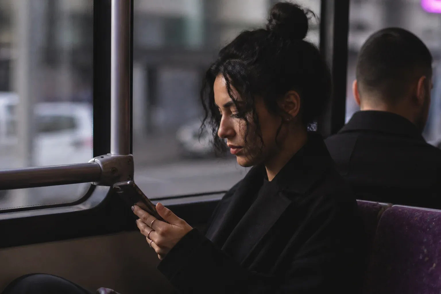 אישה על אוטובוס מחזיקה טלפון באגודל, מבט מהצד
