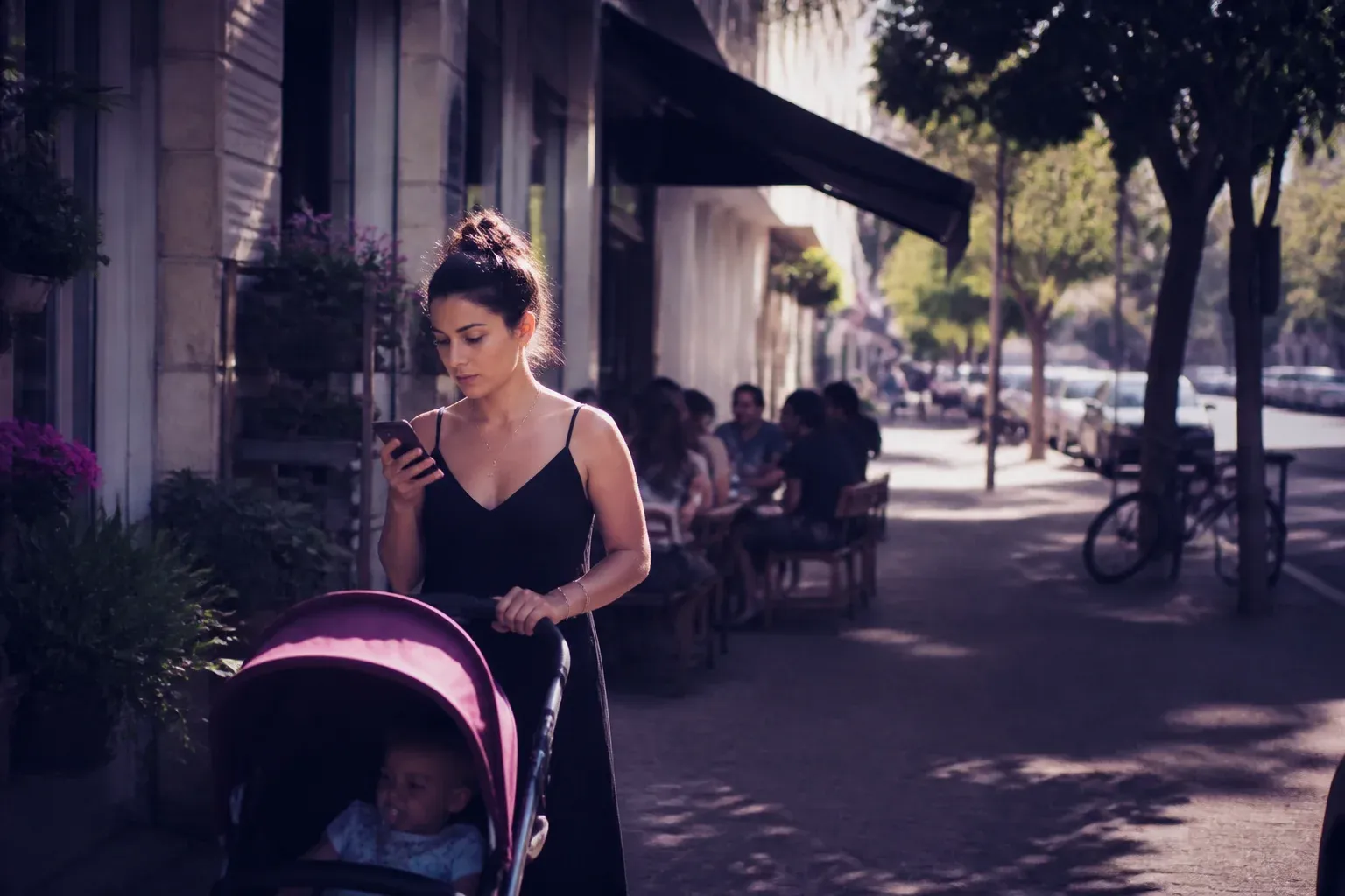 אישה עם עגלה הולכת במדרכה ובודקת טלפון בין חנויות ובתי קפה