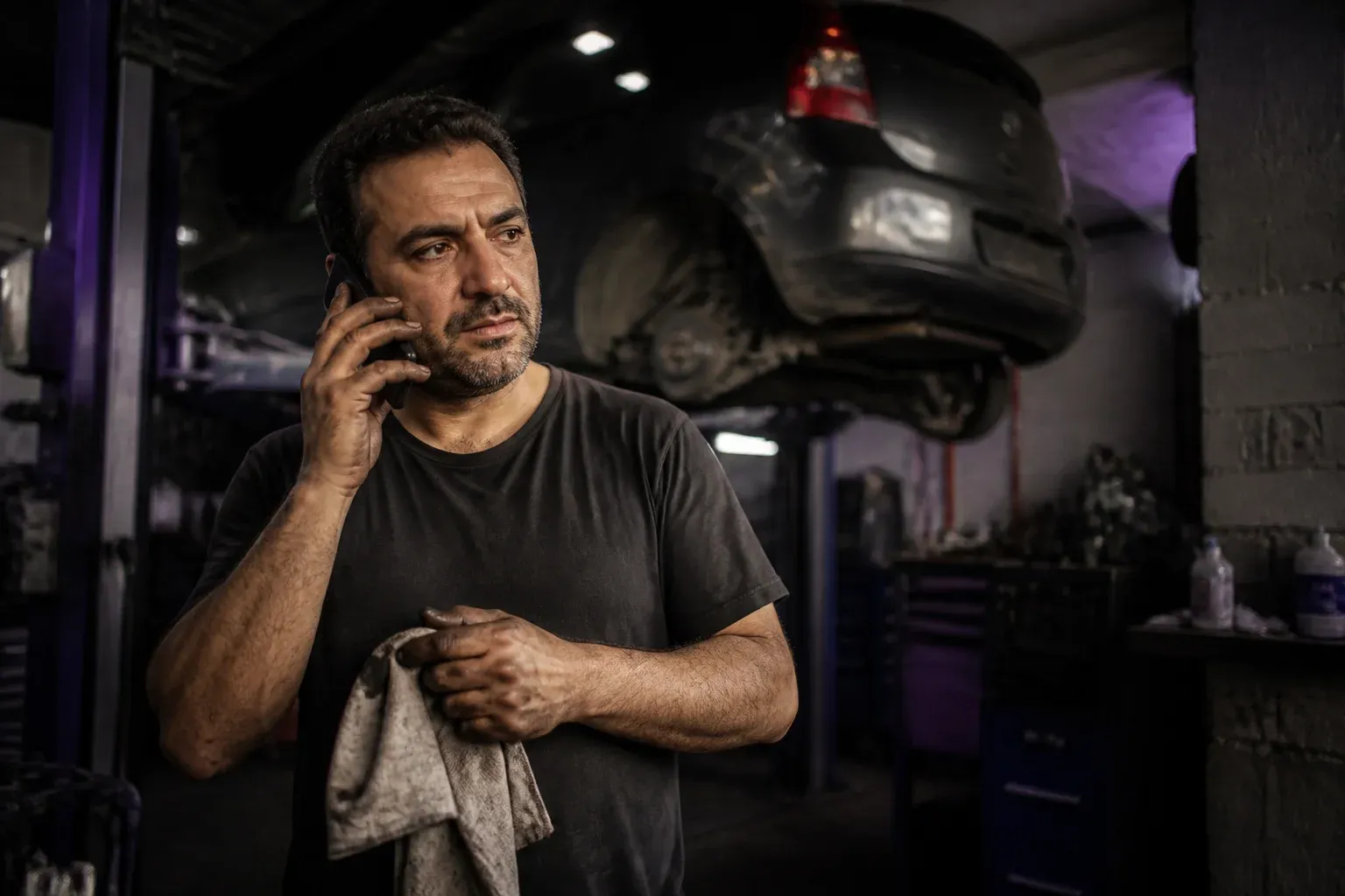 מכונאי במוסך קטן מדבר בטלפון ליד רכב על במה