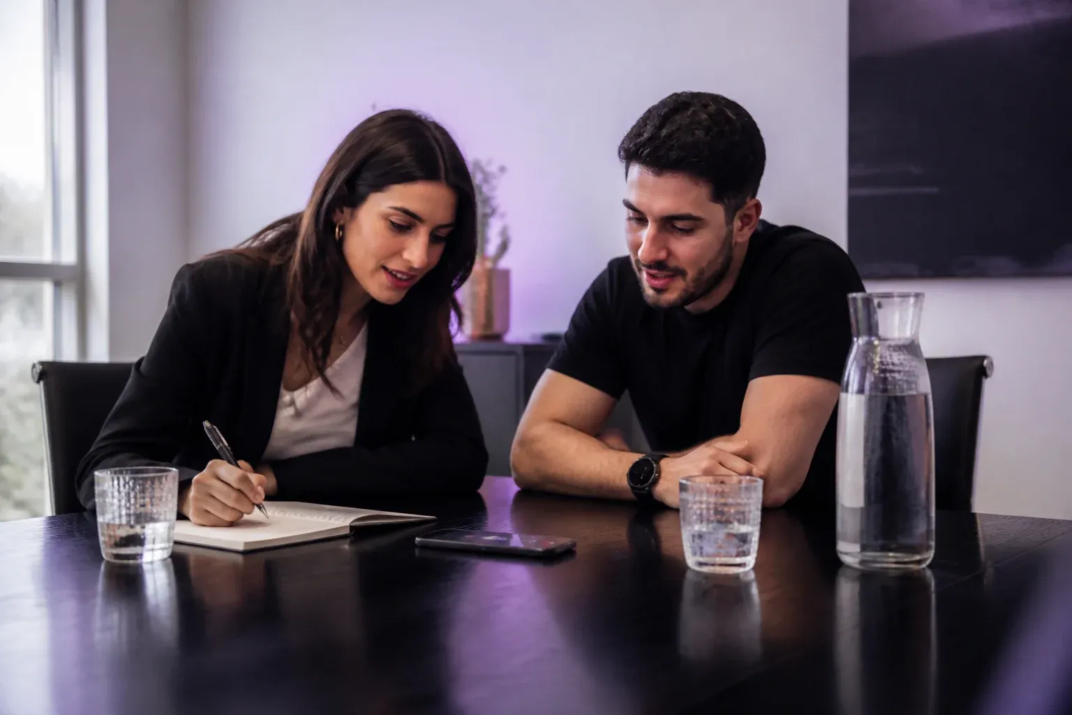 שניים נשענים לעבר טלפון על השולחן בשיחת רמקול