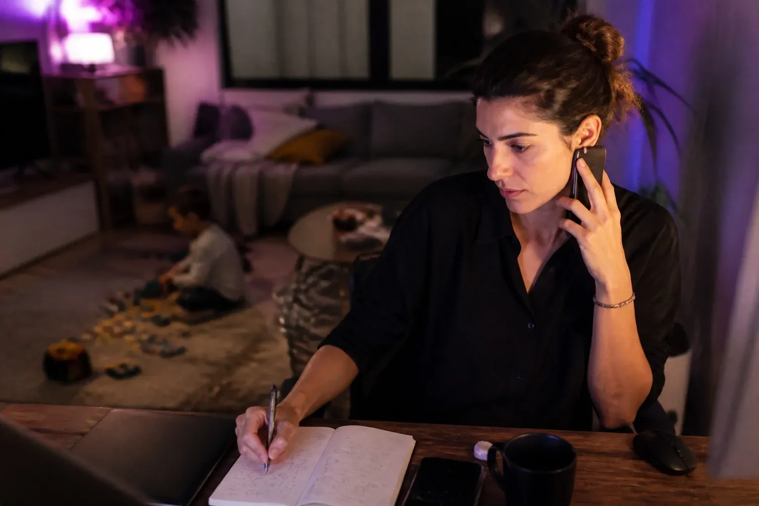 אישה עונה לשיחת עבודה בפינת עבודה בסלון, ליד צעצועים של ילד