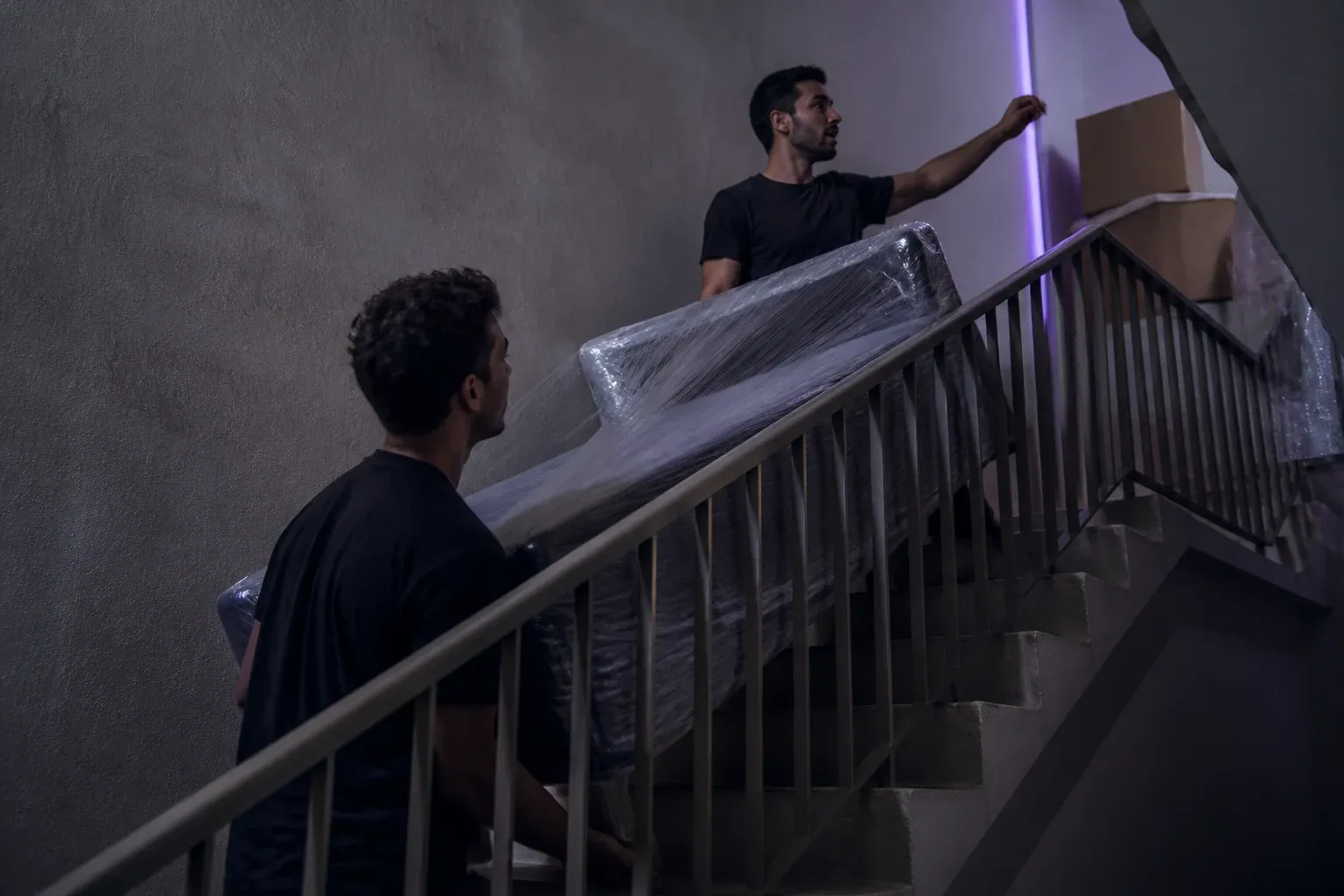 שני סבלים נושאים ספה עטופה בחדר מדרגות צר